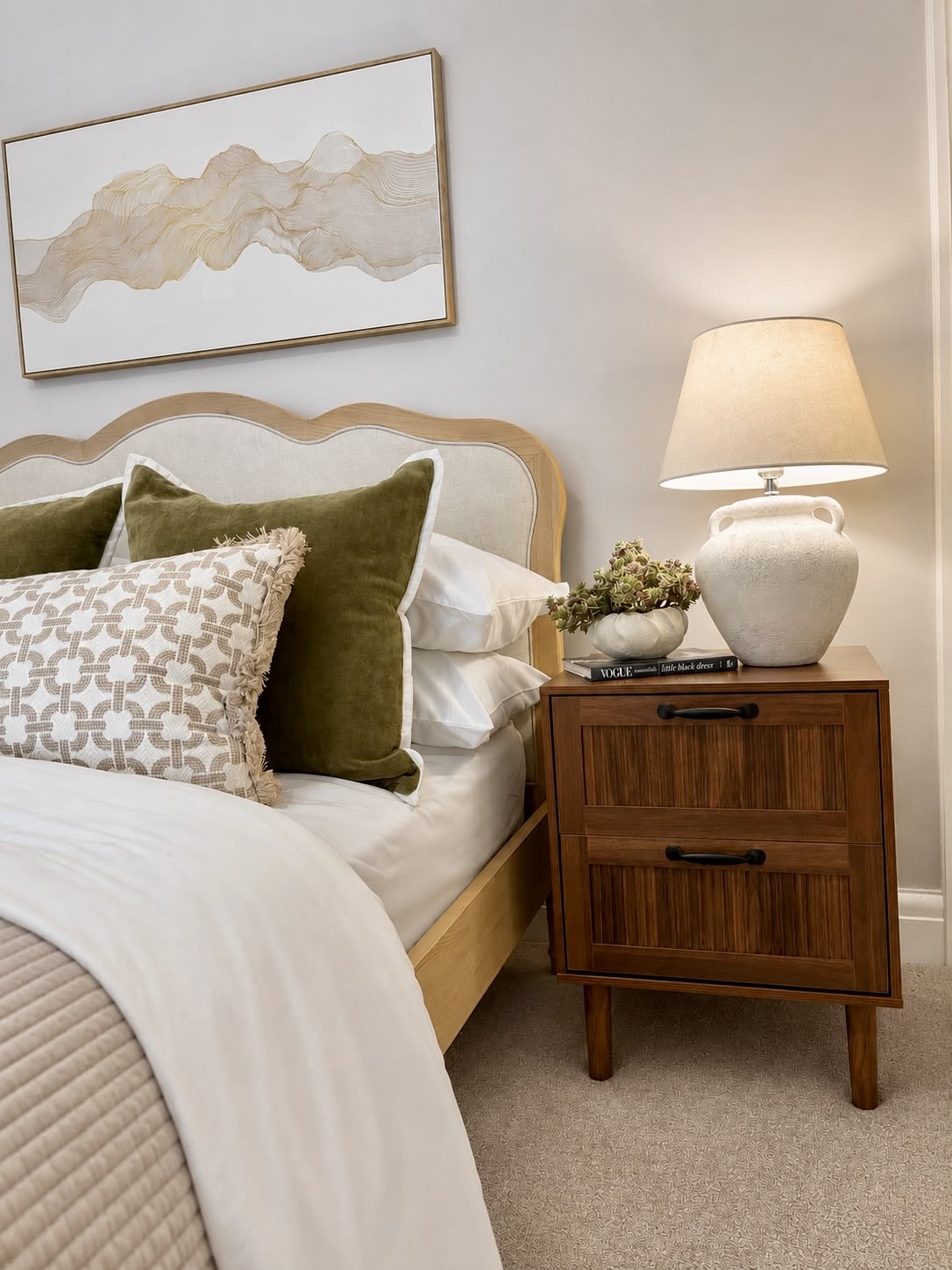 Styled bedroom with layered bedding, olive cushions and a warm bedside lamp